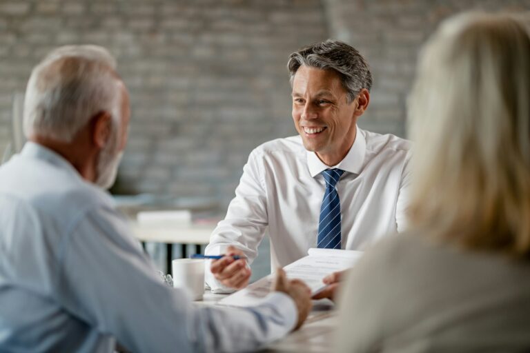 Happy bank manager talking with senior customers about terms of the contract in the office.